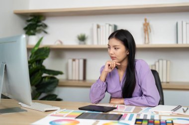 Bir grafik tasarımcısı, dijital tasarımları renk örnekleriyle çevrili bir bilgisayardan incelikle inceler..