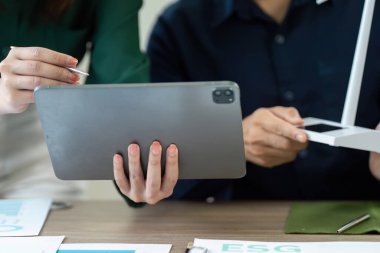 ESG strateji oturumuna katılan profesyoneller, sürdürülebilirlik girişimlerini geliştirmek için bir tablet üzerindeki verileri analiz ediyorlar.