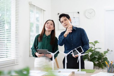 İş ortakları ESG girişimlerini tartışırken, parlak bir çalışma alanında rüzgar türbini modellerini sergiliyorlar.