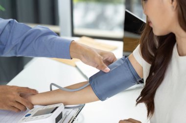 Bir sağlık hizmeti sağlayıcısı modern bir klinik ortamında sphygmomanometre kullanan bir hastanın kan basıncını ölçer..