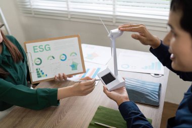 İş ortakları ESG istişaresine girişiyor, rüzgar türbini modeli sergiliyor ve sürdürülebilirlik stratejilerini tartışıyorlar.