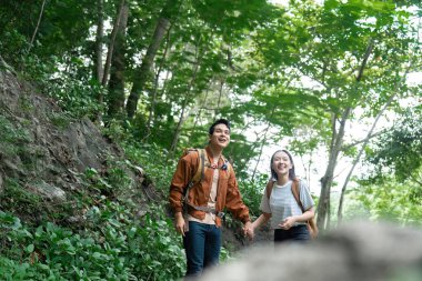 Yeşilliklerle çevrili canlı bir patika boyunca yürürken el ele tutuşan çiftler yürüyüş tecrübelerinden zevk alırlar..