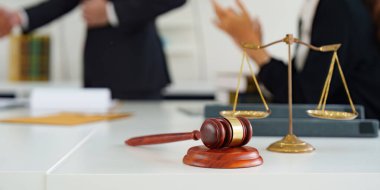 Bir tokmağın yakın çekimi ve adalet terazisi, hukuku ve adaleti simgeliyor, hukuki bir ortamda, bulanık bir el sıkışması ile.