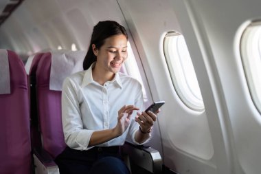 Neşeli bir iş gezgini, bir uçağın penceresinde oturan akıllı telefonuyla etkileşime girer. Kulübe parlak ve modern..