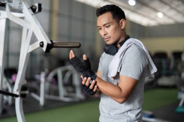 Modern bir spor salonunda egzersiz yapmadan önce bileğini düzelten odaklanmış bir adam. Sağlık ve zindelik vurgulanıyor.