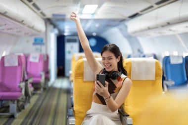 Mutlu bir bayan yolcu, seyahatin ve maceranın neşesini somutlaştıran akıllı telefonunu kullanarak bir uçakta yolculuğunu kutlar..