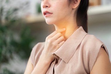 Huzursuz bir ev ortamında bir kadın nazikçe boğazına dokunuyor. Sağlık ve refahı vurgulamak.