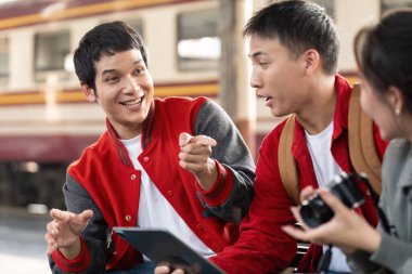 Bir grup arkadaş, bir tren istasyonunda tablet kullanırken, modern sosyal etkileşimi gösteren canlı bir tartışmaya giriştiler..