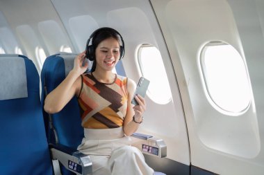 Neşeli bir bayan yolcu, uçakta otururken kulaklıklarıyla müzik dinler ve seyahatin neşesini ön plana çıkarır..