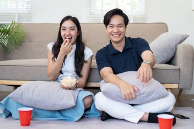 Bir çift yerde oturup film izlerken patlamış mısırın tadını çıkarıyor. Rahatlatıcı ve eğlenceli bir ortam odayı dolduruyor..