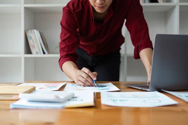 Modern bir çalışma alanındaki stratejik planlama ve analizleri vurgulayan, finansal belge ve çizelgeleri özenle inceleyen bir uzman,.