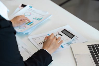 Bir muhasebeci, analiz için hesap makinesi ve çeşitli belgeler kullanan bir masanın mali raporlarını ve çizelgelerini inceler..