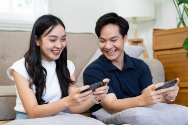 Neşeli bir çift, rahat oturma odalarında gülücüklerini ve gülücüklerini paylaşarak mobil oyunlar oynamaktan zevk alır..