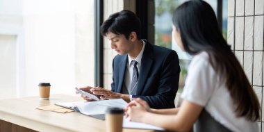 İki genç profesyonel bir kafede iş görüşmesi yapıyor, belgeleri inceliyor ve bir projede işbirliği yapıyorlar..