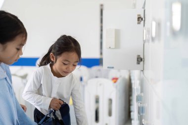 İki genç kız, okul dolaplarında arkadaşlıklarını ve okula dönüş deneyimlerini ön plana çıkarırken sohbet ediyorlar..