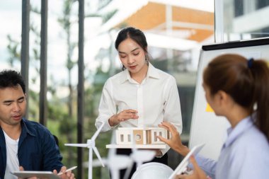 Bir kadın, iş arkadaşlarını yenilikçi mimari ve sürdürülebilirlik üzerine bir tartışmaya sokan bir yapı modeli sunar..