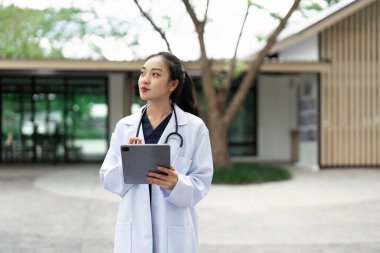 Beyaz önlüklü bir sağlık uzmanı, modern sağlık ve teknolojiyi sembolize eden açık havada tablet kullanıyor..