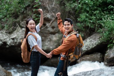 İki heyecanlı yürüyüşçü elde ettikleri başarıyı el ele tutuşarak ve güzel doğal bir fon önünde tezahürat yaparak kutluyorlar..