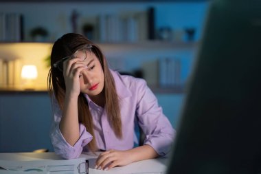 Geç saatlere kadar masasında çalışırken yorgun ve stresli görünen genç bir kadın, gece geç saatlere kadar üretkenliğin zorluklarını vurguluyor..