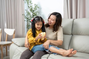 Bir anne ve kızı kanepede sıcak bir an paylaşıyor, neşeli sohbetler ve bağ kuruyor..