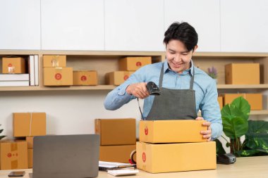 Girişimci, küçük bir işletme ortamındaki modern lojistik süreçleri vurgulayan bir barkod tarayıcı kullanarak paketleri tarar.