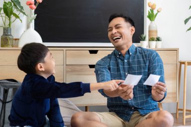 Bir baba ve oğul keyifli bir etkileşimi paylaşır, birlikte güler ve öğrenirler, aynı zamanda samimi bir ortamda kart alışverişi yaparlar..