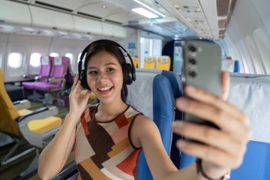 Neşeli bir gezgin uçakta otururken selfie çeker, seyahat deneyimini yakalar. Seyahat ve yaşam tarzı temaları için harika.