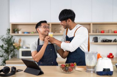 İki neşeli LGBTQ partneri bardaklarını tazeleyici bir içecekle dolduruyorlar, mutfakta birlikte vakit geçiriyorlar..