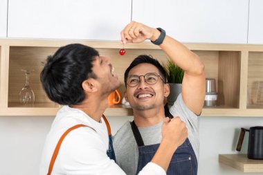 Parlak bir mutfakta iki adam şakacı bir şekilde bir kirazı paylaşıyor, ilişkilerinde sevgi ve eğlence sergiliyorlar..