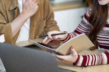 İki üniversite öğrencisi, öğrenme deneyimlerini geliştirmek için bir dizüstü bilgisayar ve bir dizüstü bilgisayar kullanarak fikir alışverişinde bulunuyorlar..