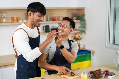 Modern bir mutfak ortamında yemek hazırlarken, aşk ve neşe sergilerken, iki adam gülüşür ve etkileşir..