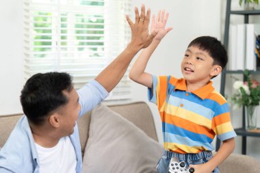 Zaferi kutlayan bir baba ve oğul, evlerindeki oyun deneyimleri sırasında güçlü bağlarını ve neşelerini sergileyerek beşlik çakar..