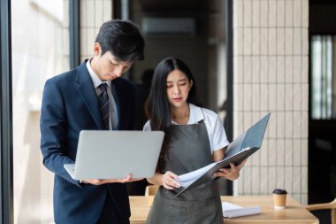Genç, profesyonel bir çift proje detaylarını bir dizüstü bilgisayarda gözden geçirir, takım çalışmasını gösterir ve çağdaş bir çalışma alanına odaklanır..
