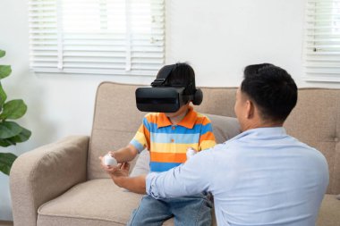 VR kulaklık takan genç bir çocuk heyecan verici bir oyun deneyimi yaşarken, babası ona destek ve cesaret veriyor..