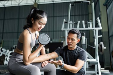 Kişisel antrenör, bayan müşteriye spor salonunda halter tekniklerini öğretir. Güç antrenmanı ve formda kalmayı teşvik eder..