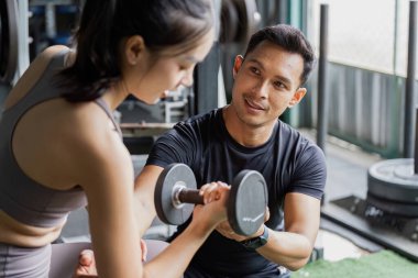 Kendini adamış bir özel antrenör, spor salonunda halter egzersizinde bir kadına yardımcı olur..
