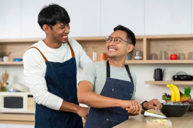 İki adam, şık bir mutfak ortamında yemek pişirirken, aşk ve takım çalışmasını sergilerken, neşeli bir anı paylaşıyor..