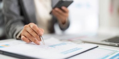 Akıllı telefon kullanırken raporlara ilişkin verileri analiz eden odaklanmış bir birey, profesyonel bir ortamda birden fazla görevi vurgular.