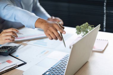 İki profesyonel, önemli veri ve belgeleri incelerken bir dizüstü bilgisayarı işaret ederek işbirliği yapıyor..