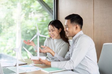 İki meslektaş sürdürülebilir enerji çözümleri hakkında canlı bir tartışmaya girişerek, parlak bir çalışma alanında bir rüzgar türbini modeli sergilediler..