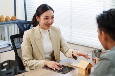 Profesyonel bir emlakçı müşterisiyle mülkiyet seçeneklerini tartışıyor, modern bir ofiste dostane ve çekici bir atmosfer sergiliyor..