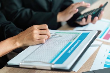 Bir şirket ortamında takım çalışması ve analitik tartışmaları vurgulayan bir mali rapor üzerinde işbirliği yapan iki iş adamı.