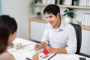 Bir emlakçı, modern ofis ortamında mülkiyet tercihleri hakkında fikir ve tavsiyelerde bulunan bir müşteriyle ilişki kurar..