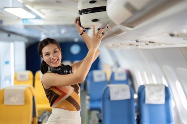 Kulaklıklı neşeli bir bayan yolcu, hava yolculuğunun sevincini göstermek için valizini bir uçağın tepesindeki kutuya koyuyor..