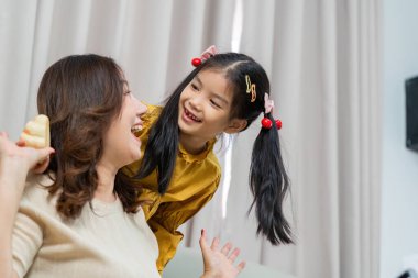 Bir anne ve kızı neşeli bir anı paylaşıyor, gülümsüyor ve kapalı bir ortamda birlikte oynuyorlar..