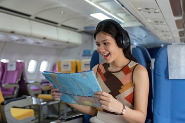 Mutlu bir gezgin uçakta bir harita okurken, rahatlık ve macerayı harmanlarken müzik dinler. Seyahat ve yaşam tarzı temaları için mükemmel.