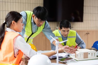 Bir model ve rüzgar türbini ile yenilenebilir enerji çözümlerine odaklanan sürdürülebilir bir inşa projesini tartışan çeşitli bir mühendis grubu.