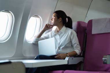 Uçuş sırasında dizüstü bilgisayarıyla uğraşan odaklanmış bir iş kadını modern seyahat yaşam tarzını yansıtıyor..
