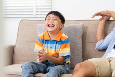 Bir baba ile oğul arasında neşeli bir an, evdeki rahat bir kanepede kahkaha ve mutluluğu paylaşıyorlar..