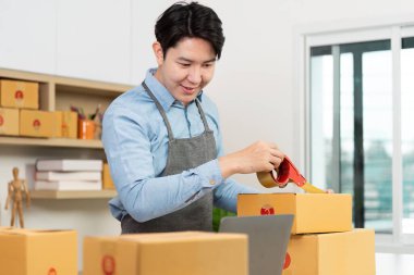 Girişimci paketleri dikkatlice bant ile mühürler, detaylara dikkat eder ve hareketli bir ofis ortamında verimli nakliyeye bağlılığını gösterir.